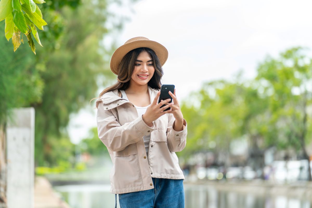 eSIM im Ausland: Frau hält ihr Smartphone in den Händen und trägt Urlaubskleidung.